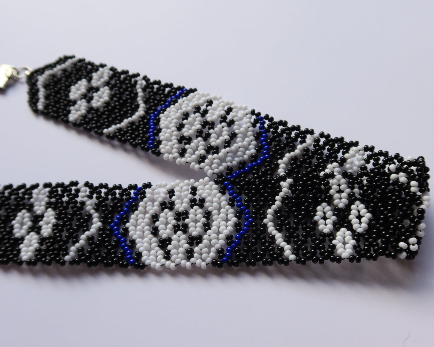 Beaded belt with black, white, and blue pattern on a light gray background