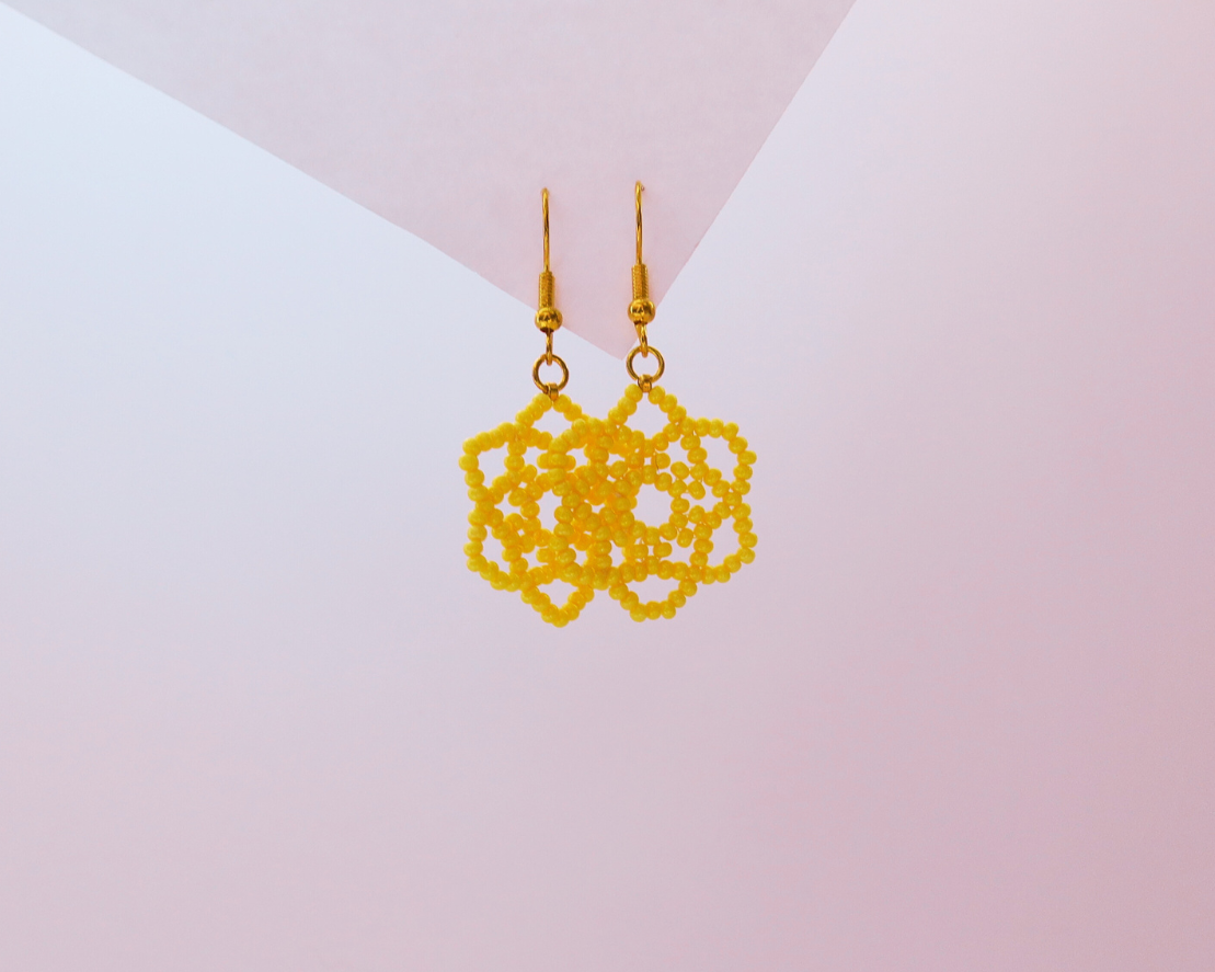 Gold lace-style earrings on a gradient pink and white background