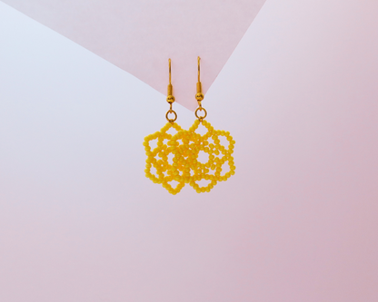 Gold lace-style earrings on a gradient pink and white background