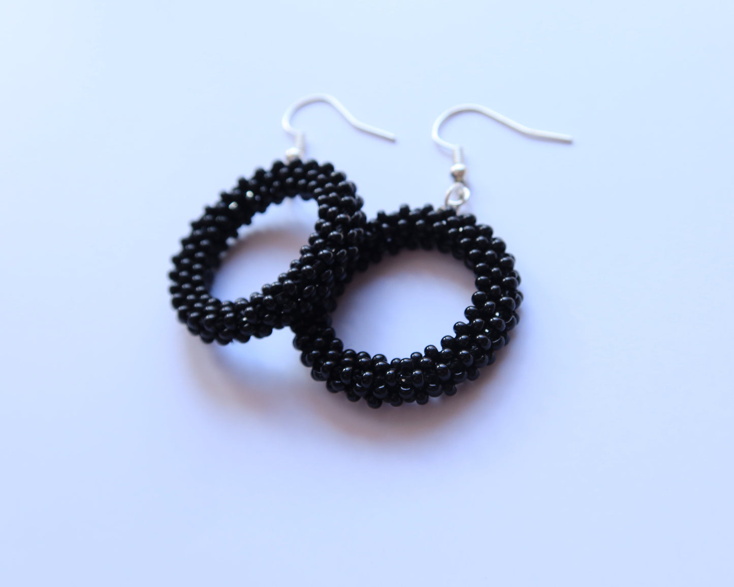 Black beaded hoop earrings on a light blue background