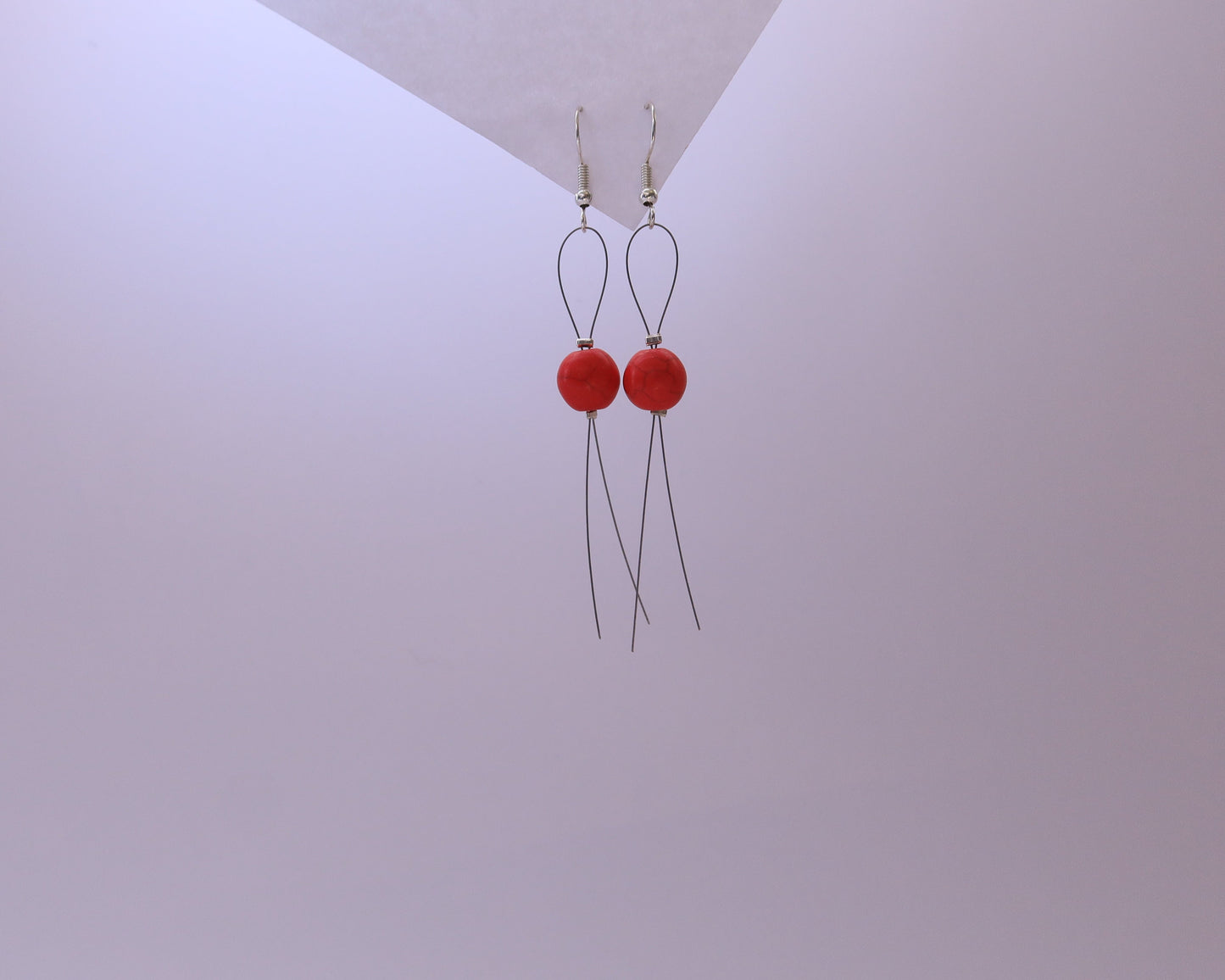 Red earrings with long thin wires on a light gray background