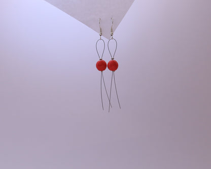 Red earrings with long thin wires on a light gray background