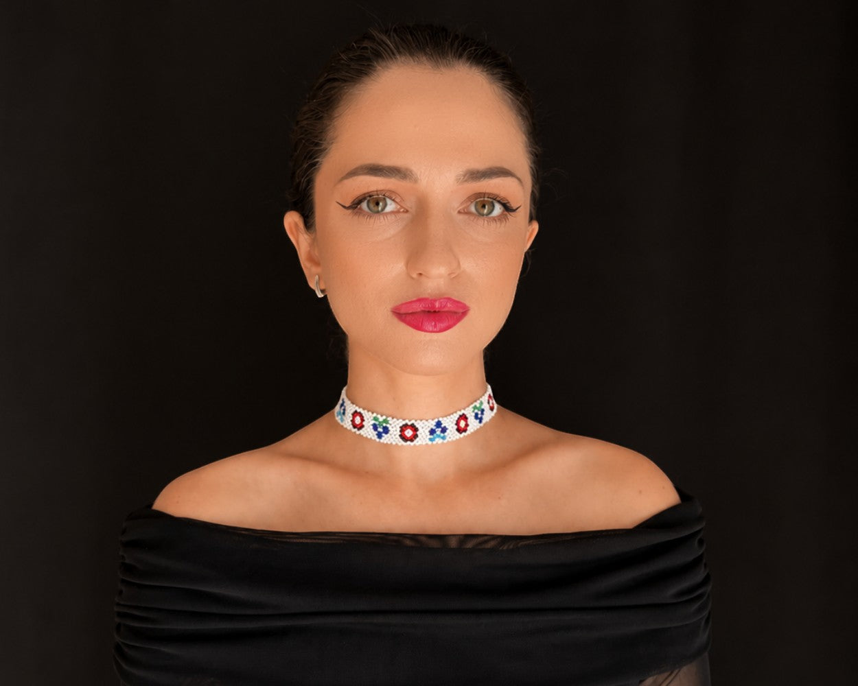 Comely UA white beaded choker with floral motifs in red, blue, and green. Adjustable velvet ribbon closure.