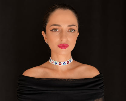 Comely UA white beaded choker with floral motifs in red, blue, and green. Adjustable velvet ribbon closure.