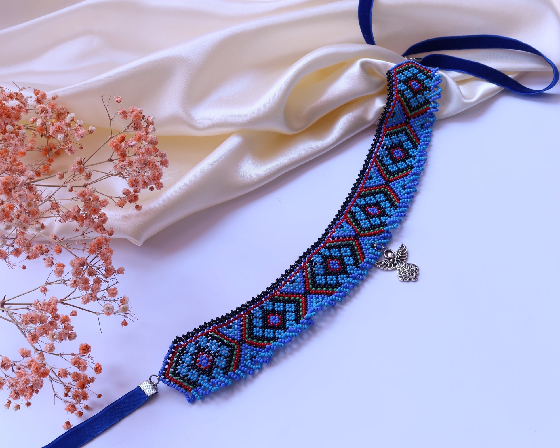 Comely UA beaded choker with blue, black, and red geometric pattern and angel charm. Velvet ties.