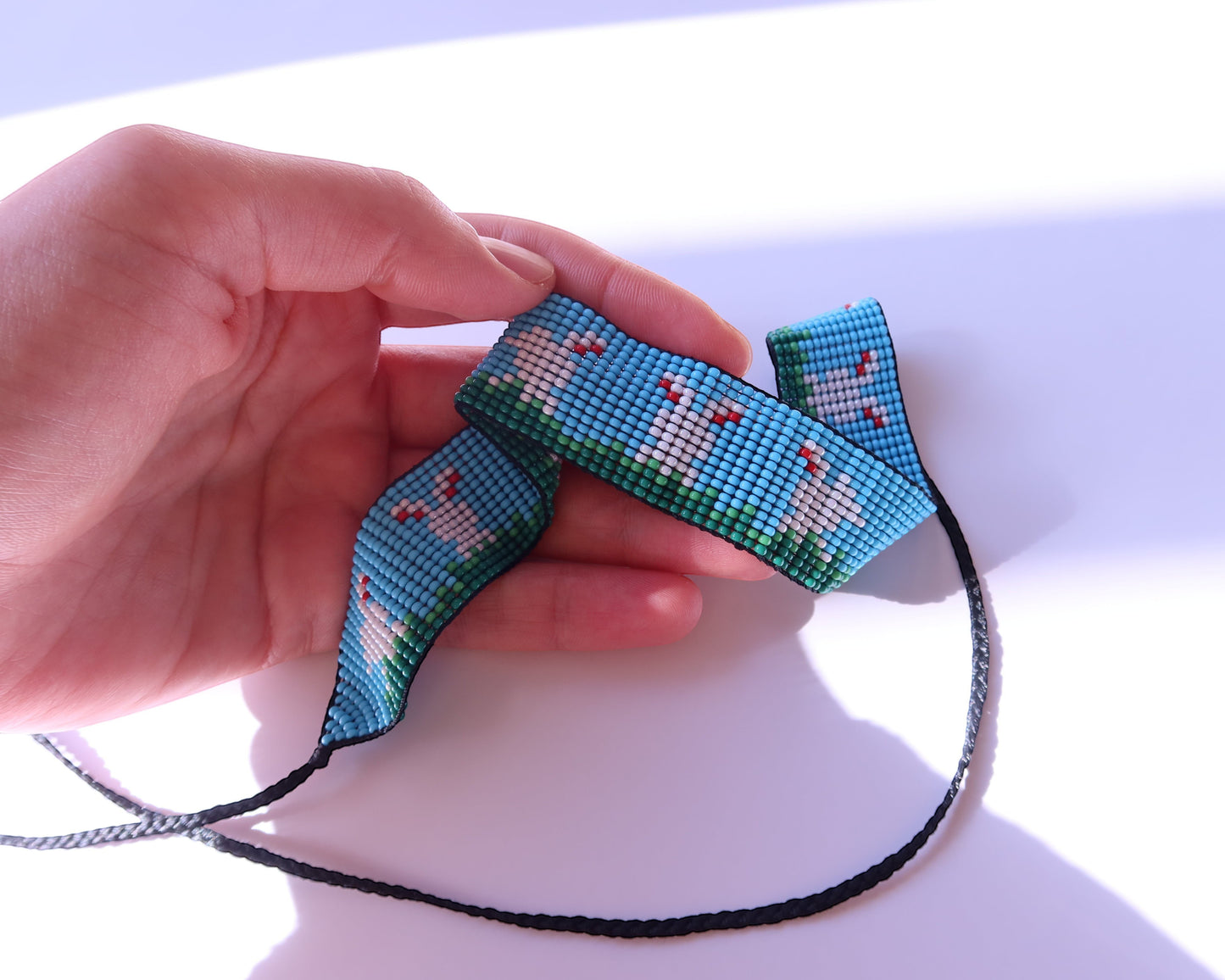 Comely UA beaded gerdan with white hares and green grass on a blue sky background. Adjustable ties with tassels.