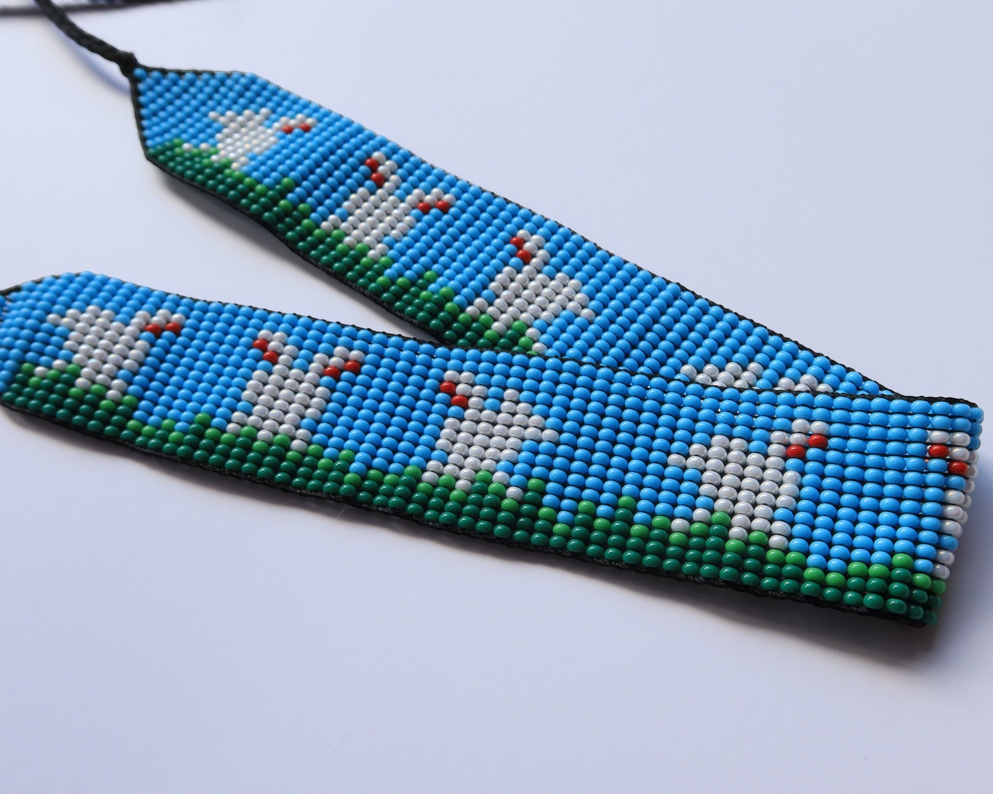 Comely UA beaded gerdan necklace with white hares and green grass on a blue sky background. Adjustable ties with tassels.