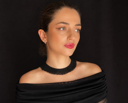 Comely UA black beaded silyanka necklace, a flat woven choker with a geometric pattern, worn by a woman against a black background.
