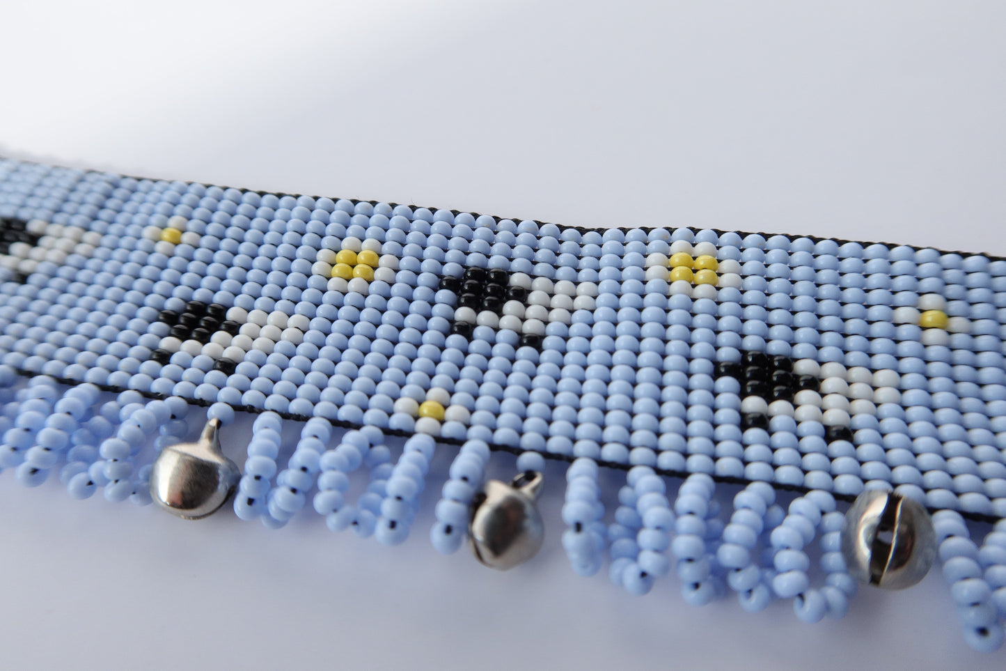 Comely UA light blue beaded gerdan with white daisies, black and white sheep, and yellow accents. Features a fringe with silver bells.