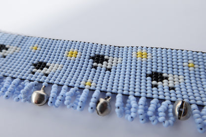 Comely UA light blue beaded gerdan with white daisies, black and white sheep, and yellow accents. Features a fringe with silver bells.