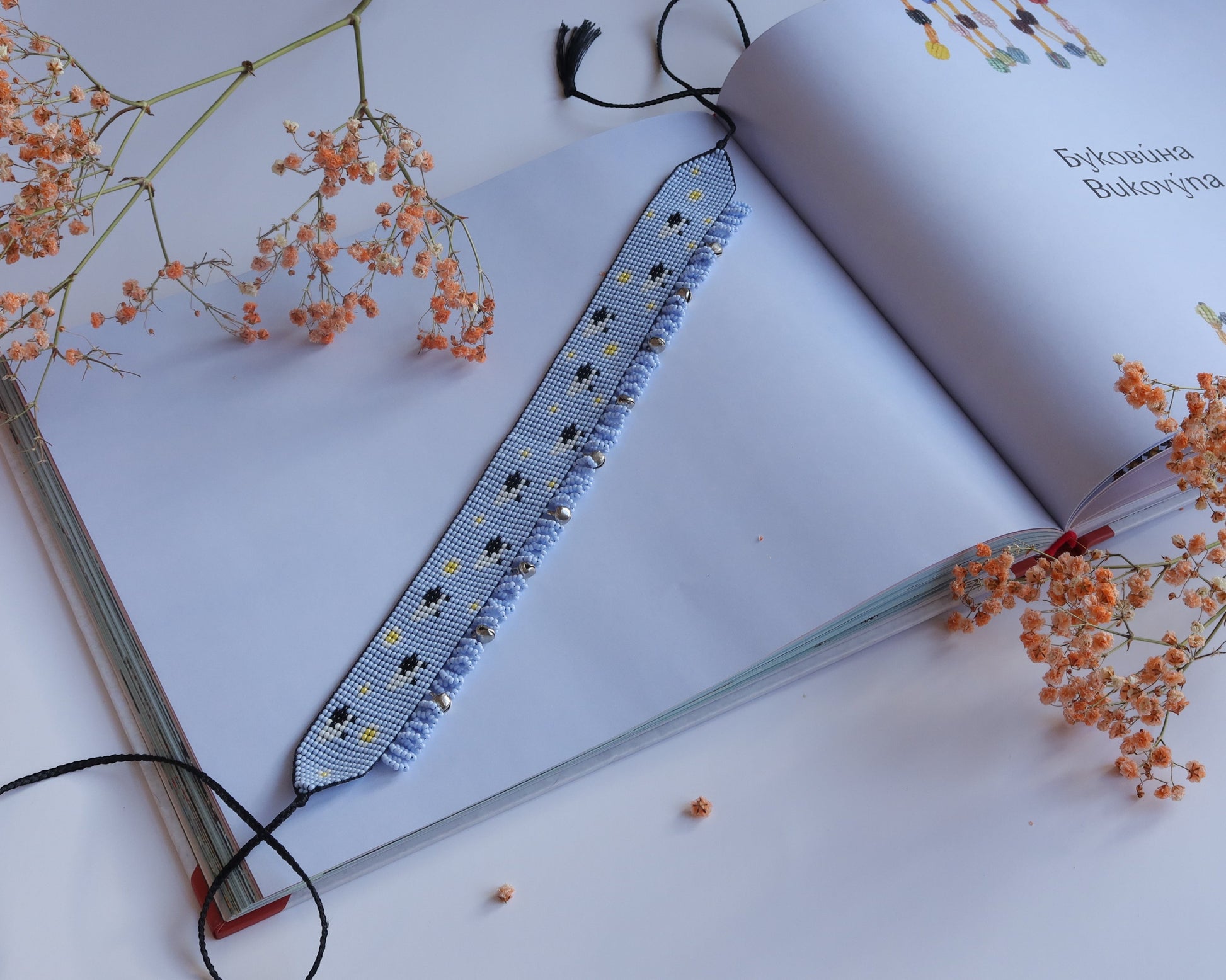 Comely UA light blue beaded gerdan with white daisies and sheep pattern, featuring silver bead fringe and black tassels.
