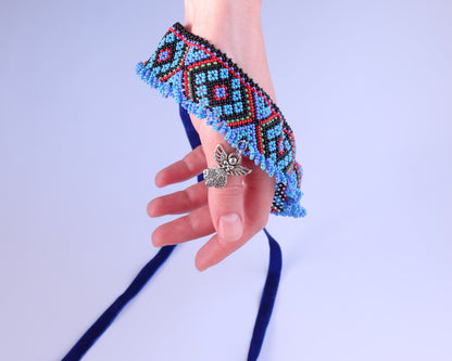 Comely UA Gerdan Luchka beaded collar with blue, black, red, and green geometric pattern and fringe. Features an angel pendant.