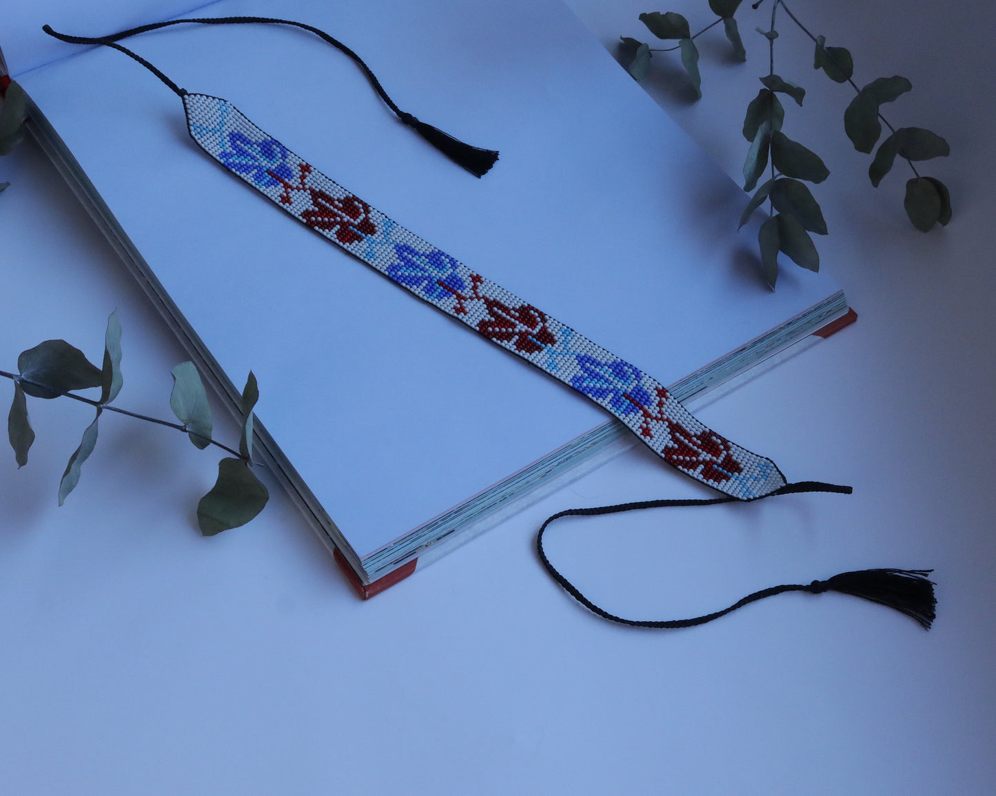 Comely UA beaded gerdan necklace with blue and red leaf pattern on white background. Tassel-ended cords.