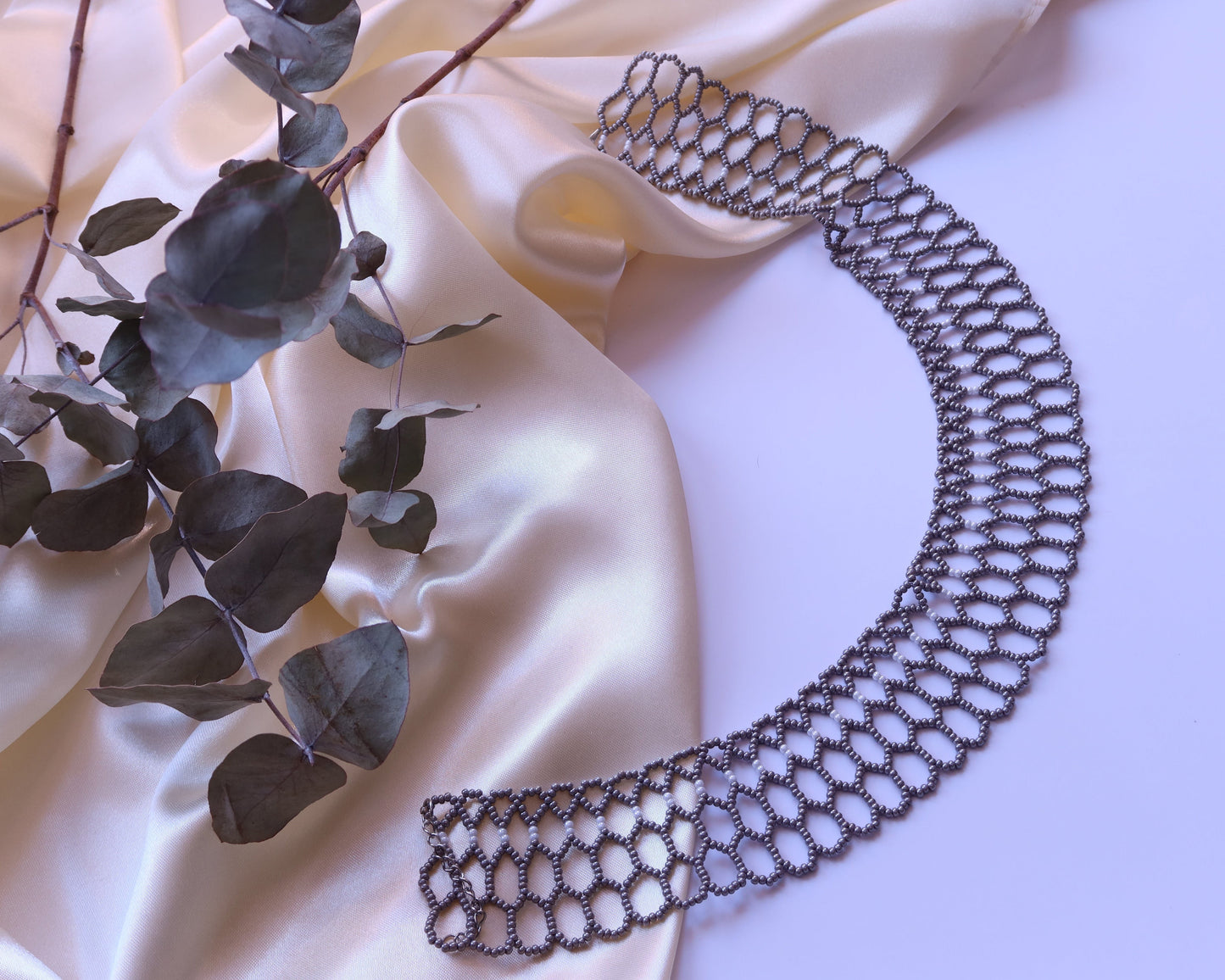 Comely UA Silyanka "Bee Nest" choker necklace, silver-gray Czech seed beads, openwork honeycomb design, on cream satin with eucalyptus branch.