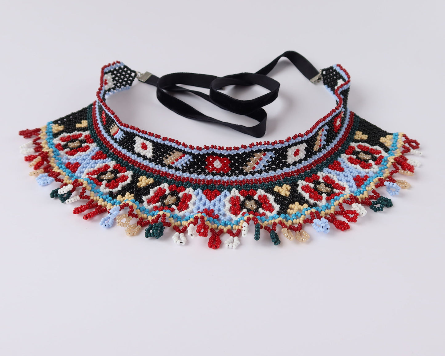 Comely UA two-part Silyanka Ladder beaded choker necklace with red, blue, black, white, and yellow floral and geometric patterns. Features fringe detail and black velvet ribbons.