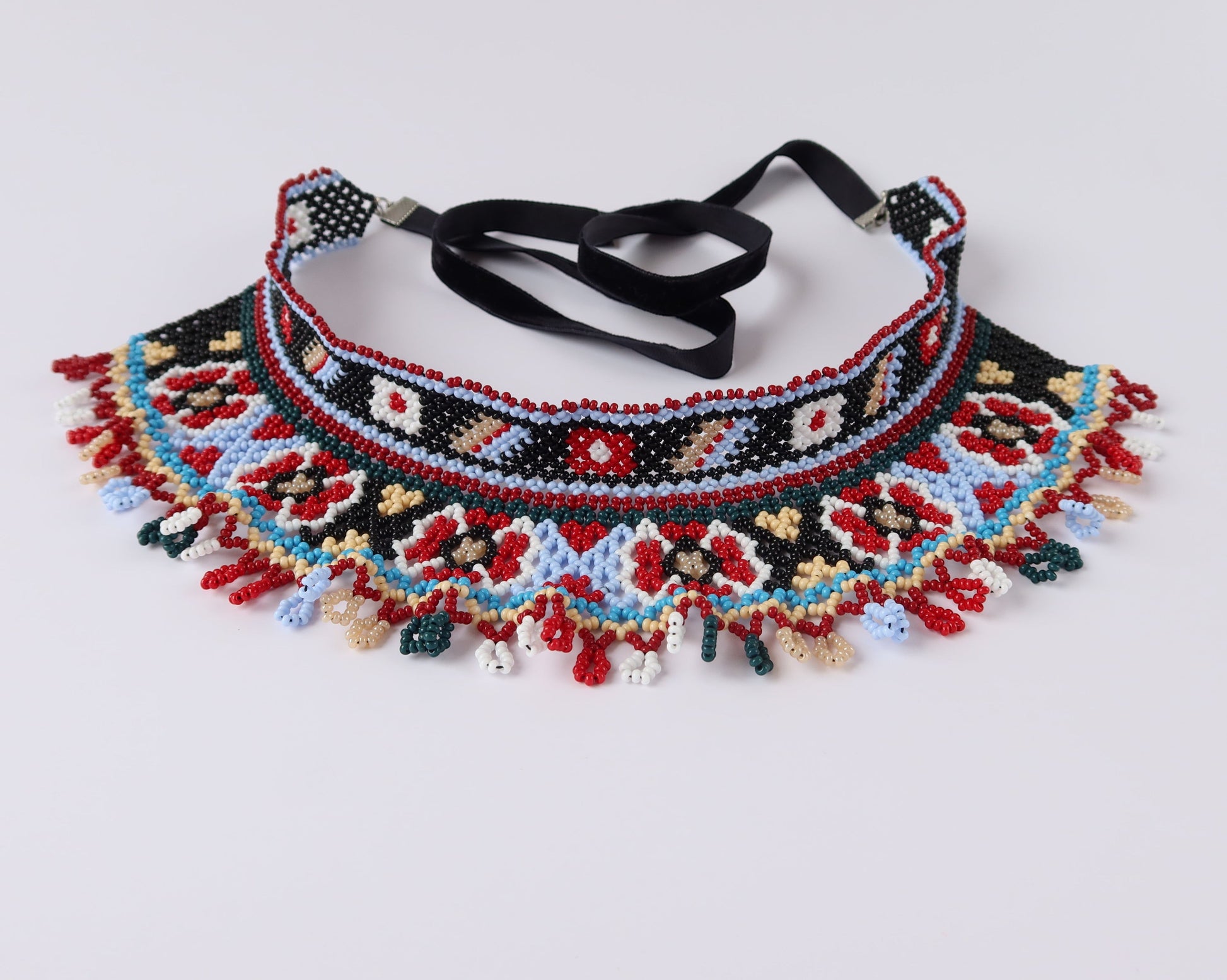 Comely UA two-part Silyanka Ladder beaded choker necklace with red, blue, black, white, and yellow floral and geometric patterns. Features fringe detail and black velvet ribbons.