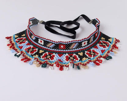 Comely UA two-part Silyanka Ladder beaded choker necklace with red, blue, black, white, and yellow floral and geometric patterns. Features fringe detail and black velvet ribbons.