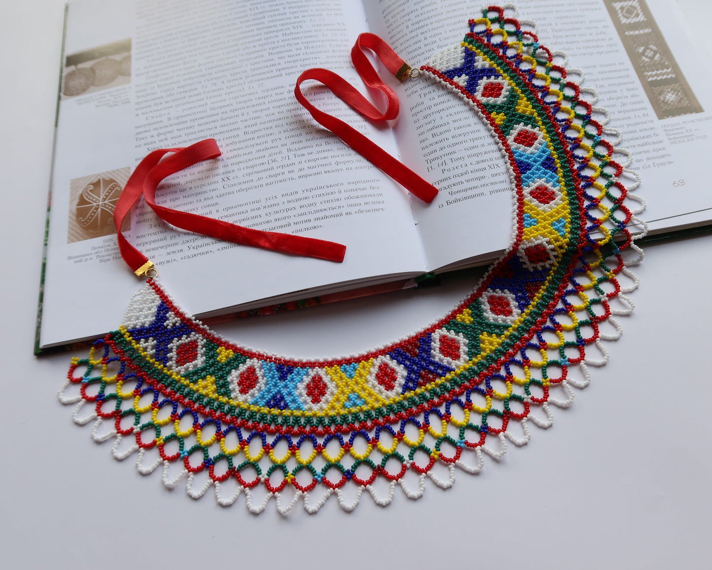 Comely UA Silyanka Lado beaded necklace with diamond and cross motifs in red, blue, yellow, green, and white. Features a delicate openwork lattice edge and red velvet ties.