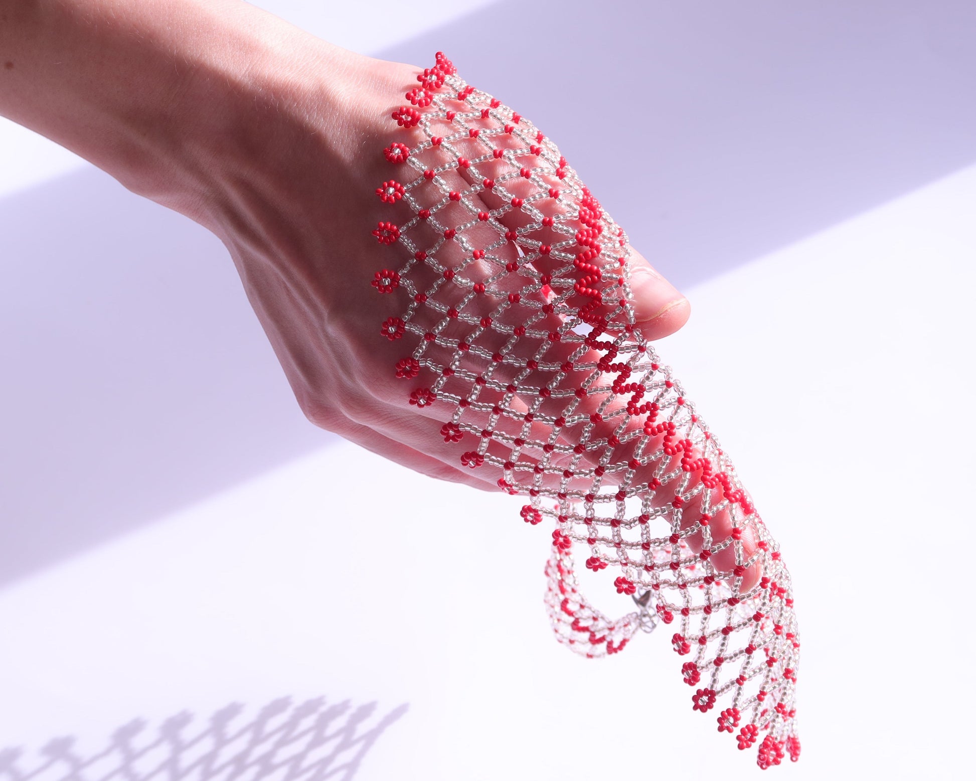 Comely UA Silyanka Solar Crown beaded bracelet with red floral accents on a silver web, worn on a hand.
