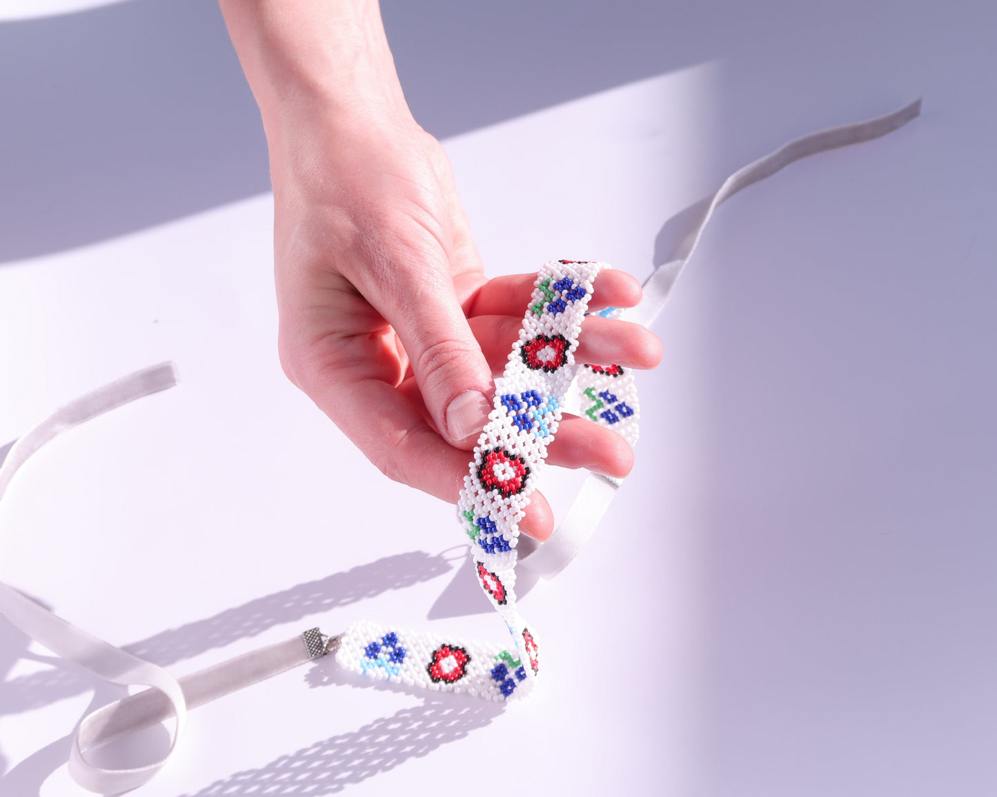 Comely UA white beaded gerdan necklace with red, blue, and green floral motifs and velvet ribbon ties.