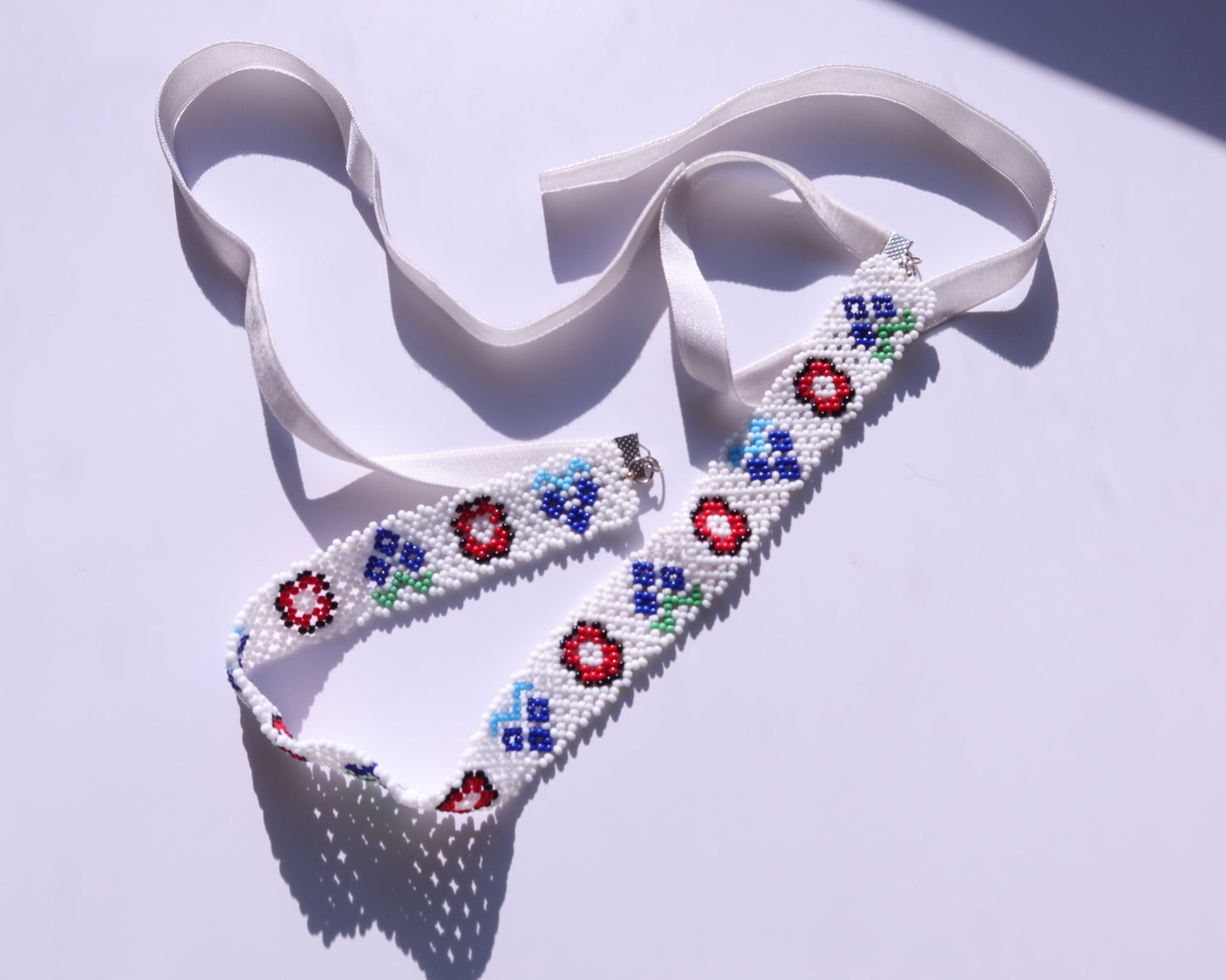 Comely UA white beaded gerdan necklace with red, blue, and green floral motifs and white velvet ribbons.