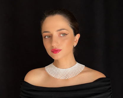 Comely UA white beaded silyanka necklace, a flat choker with a net-like pattern, worn by a woman against a black background.