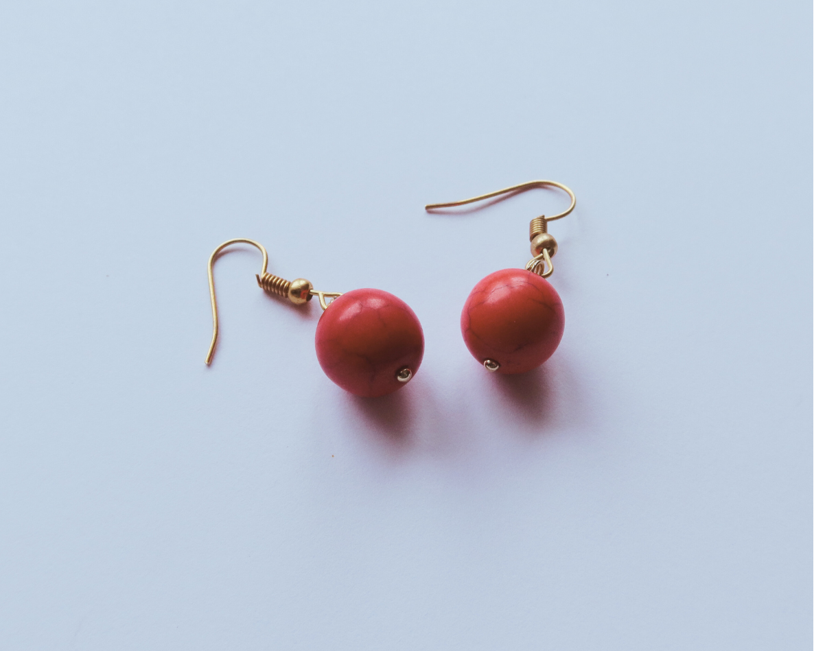 Red earrings with gold hooks on a light blue background