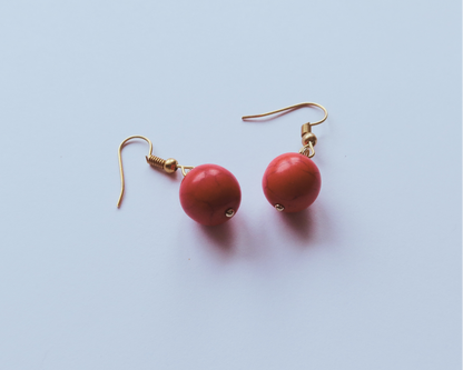 Red earrings with gold hooks on a light blue background