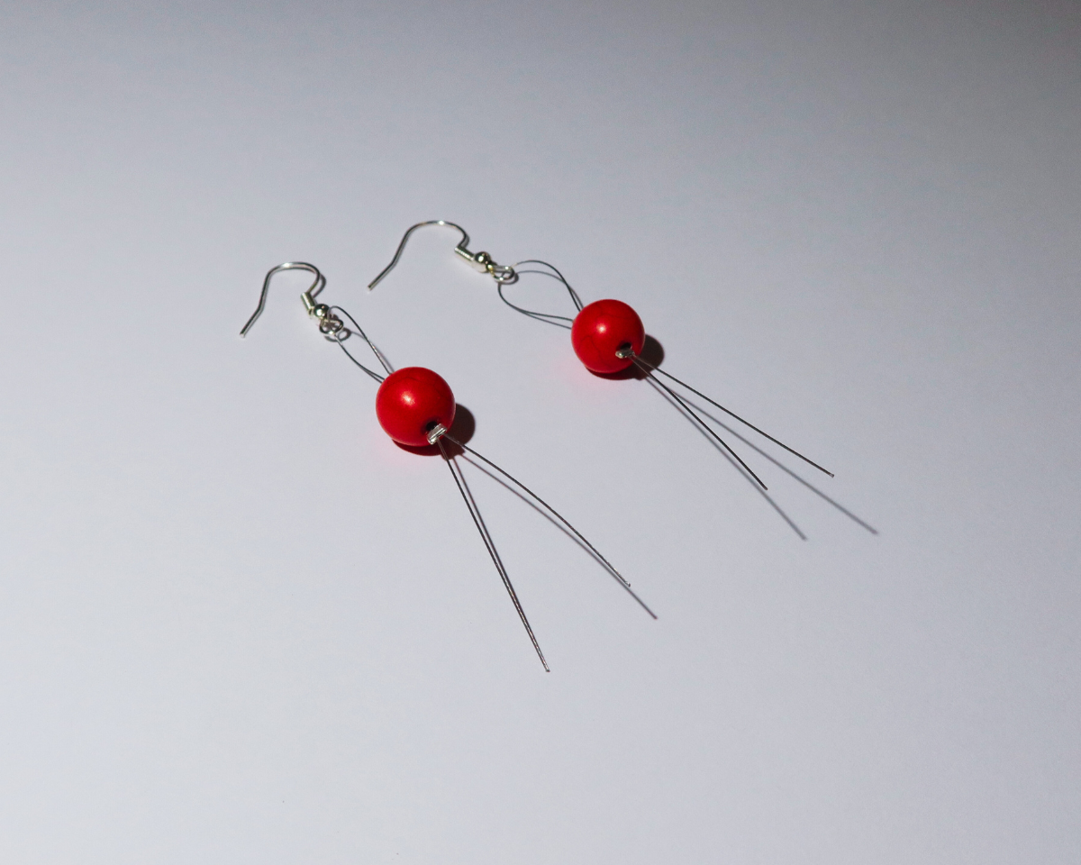 Pair of earrings with red beads and thin wires on a light gray background